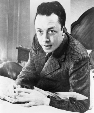 Albert_Camus,_gagnant_de_prix_Nobel,_portrait_en_buste,_posé_au_bureau,_faisant_face_à_gauche,_cigarette_de_tabagisme